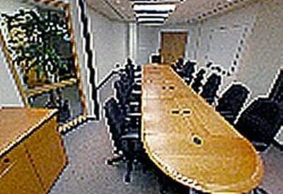 Long wooden boardroom table surrounded by black ergonomic chairs in a narrow meeting room.