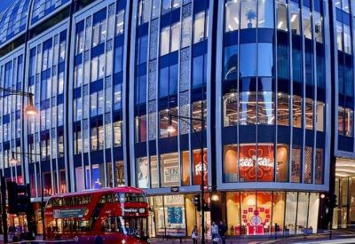 Modern glass-fronted commercial building with a red double-decker bus passing by.