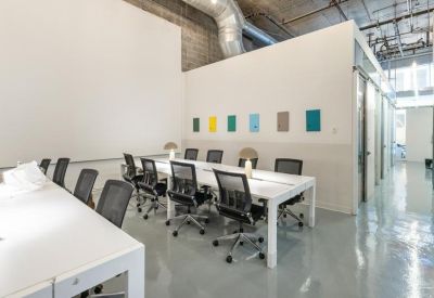 Long white communal work table with ergonomic mesh chairs in a bright, modern open-plan office.