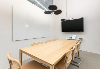 Minimalist conference room featuring a light wood table, stylish chairs, and a large wall-mounted screen.