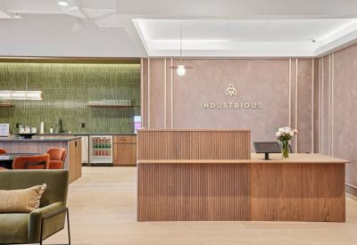 Reception area with a light wood desk, branded dusty pink wall, and floral arrangement.