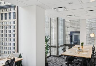 Bright workspace with a large wooden communal desk, black mesh chairs, and floor-to-ceiling windows.