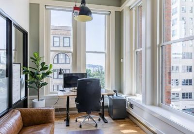 Private office with a wooden desk, leather sofa, and large windows with city views.