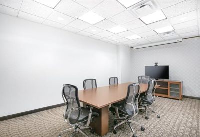 Professional conference room with a wooden table, six mesh chairs, and a wall-mounted TV.