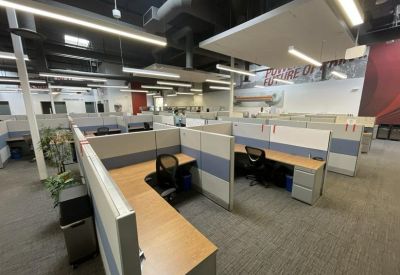 Spacious open-plan workspace featuring rows of modern cubicles and industrial-style lighting.