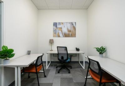 Internal three-person office suite with white desks, orange-accented chairs, and framed wall art.