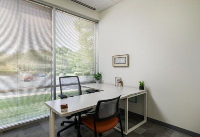 Bright window office with an L-shaped desk and views of a green parking area.