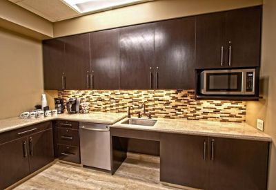 Modern communal kitchen with dark wood cabinetry and stone backsplash.