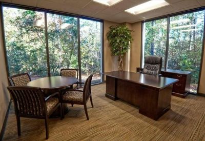 Private office with large windows overlooking trees and a wooden desk.