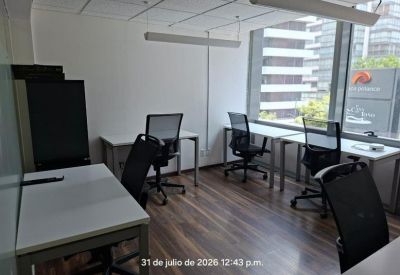 Bright shared office space with multiple workstations and large windows.