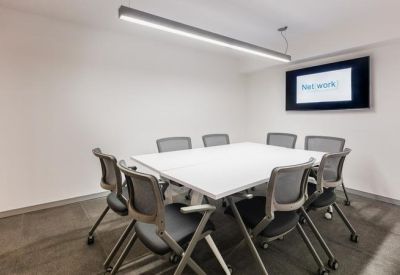 Sleek minimalist boardroom with a white table and wall-mounted screen.