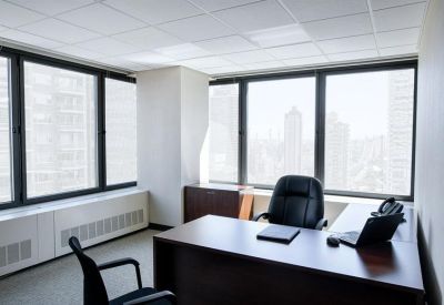 Private corner office with a dark wood desk and large windows overlooking city skyscrapers.