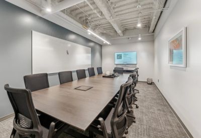 Modern conference room with a large wooden table, black chairs, and a mounted display screen.