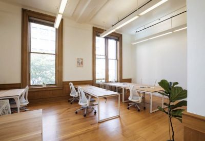 Bright office space with multiple white desks, ergonomic chairs, and large historic windows.