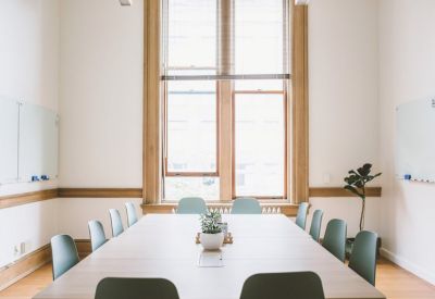 Bright conference room with a large table, light blue chairs, and a whiteboard by tall windows.