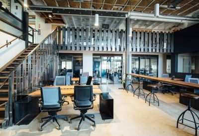 Spacious industrial coworking area with wooden desks, ergonomic chairs, and a mezzanine level.