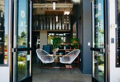 Glass entrance doors open to a lobby with white wicker chairs and indoor plants.