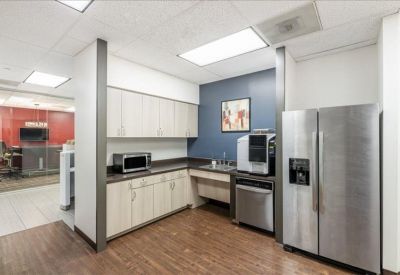 Modern office kitchen with wood-look flooring and stainless steel appliances.