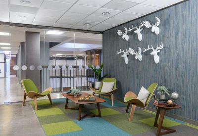 Breakout lounge with green armchairs, a geometric rug, and decorative white deer heads on a blue feature wall.