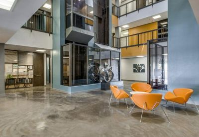 Spacious multi-level atrium lobby with polished concrete floors and bright orange modern lounge seating.