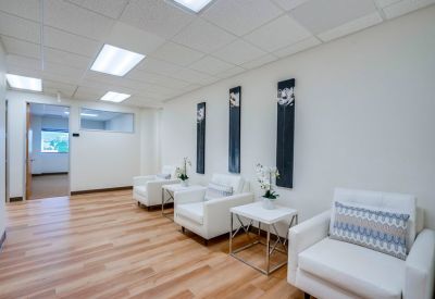 Waiting area with white armchairs, wood-style flooring, and contemporary wall art.