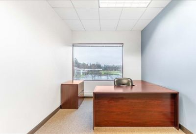Private office with a large window overlooking a pond and a wooden L-shaped desk.