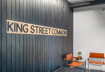 Signage for King Street Commons on a dark wood-paneled wall with orange seating nearby.