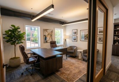 Private office suite featuring two wooden desks, a patterned rug, and a large potted plant.