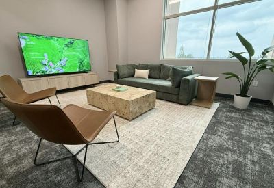 Modern lounge area with a green sofa, tan armchairs, and a large wall-mounted TV.