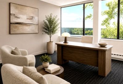 Bright private executive office with plush armchairs, wooden desk, and large windows.