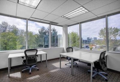 Sun-drenched corner office featuring three mesh chairs and two white minimalist desks.