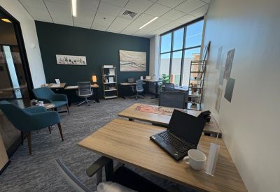 Private office suite featuring a dark accent wall, two wooden desks, and comfortable teal armchairs.