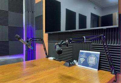 Professional podcast studio with acoustic wall panels, microphones, and a large wooden table.