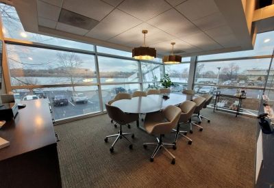 Bright conference room with an oval table, modern grey chairs, and large windows overlooking the city.
