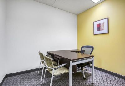 Small private office with a wooden L-shaped desk and a yellow feature wall.