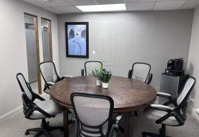 Modern meeting room featuring a round wooden table, mesh chairs, and a coffee station.