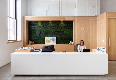 Modern reception area with a white desk and a branded green moss feature wall.
