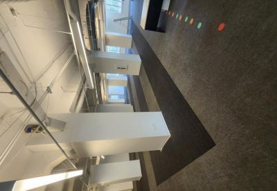 Wide view of a bright office corridor with white pillars and exposed industrial ceiling.