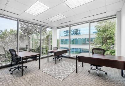 Bright corner office suite with three wooden desks and floor-to-ceiling windows.