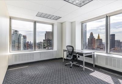 Bright corner office with a black mesh chair and expansive city views through two large windows.