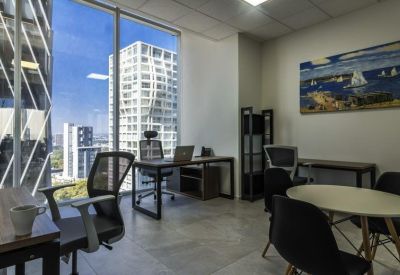 Private office with desk, ergonomic chair, and floor-to-ceiling windows showing city views.