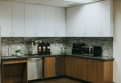 Modern office kitchen with wood cabinets, white upper cupboards, and a mosaic backsplash.