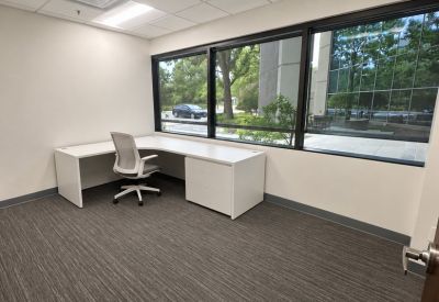 Private office featuring white furniture and large windows overlooking lush green trees.