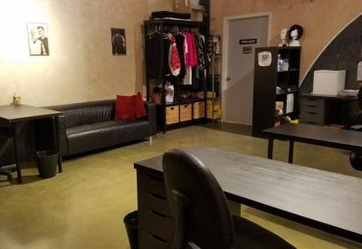 Spacious office workspace with a black leather sofa, red pillow, and multiple workstations.