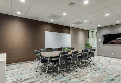 Spacious conference room featuring a long wooden table, black leather chairs, and colorful carpet.