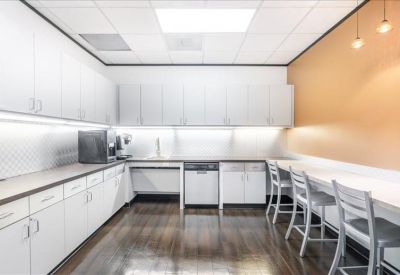 Modern breakroom with white cabinetry, a long dining counter, and warm orange accent wall.
