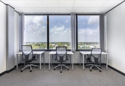 Bright shared office space with three desks facing large windows with green views.