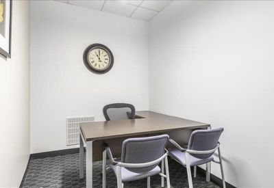 Private office suite with a corner desk, round wall clock, and three chairs.