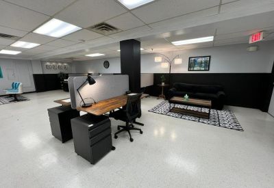 Modern office interior with wooden desks, black chairs, and a cozy lounge area with a sofa.