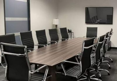 Spacious boardroom with a long wood-finish table and black leather chairs.